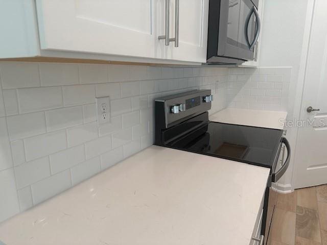 kitchen featuring white cabinetry, stainless steel electric range, decorative backsplash, and light wood-type flooring