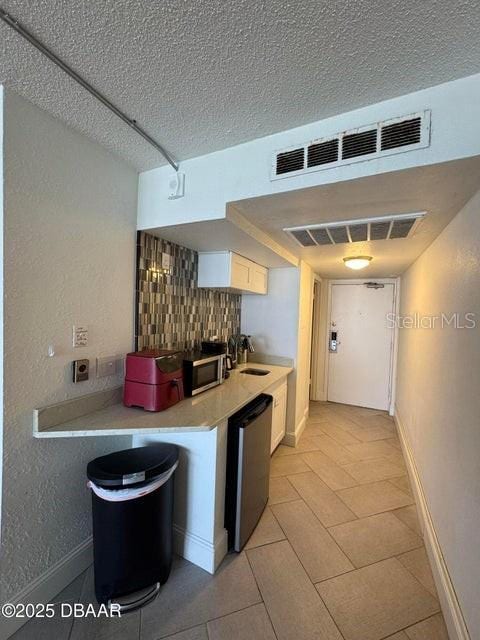 kitchen featuring a textured ceiling, dishwashing machine, white cabinetry, sink, and backsplash