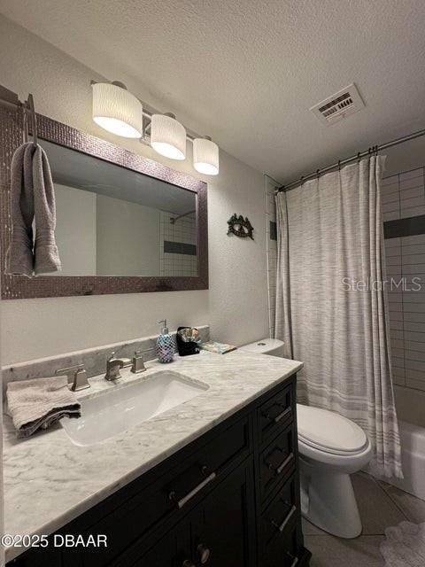 full bathroom featuring toilet, a textured ceiling, shower / tub combo with curtain, tile patterned flooring, and vanity