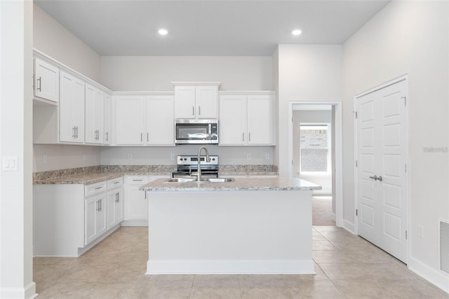 kitchen with white cabinets, light stone counters, a center island with sink, and appliances with stainless steel finishes