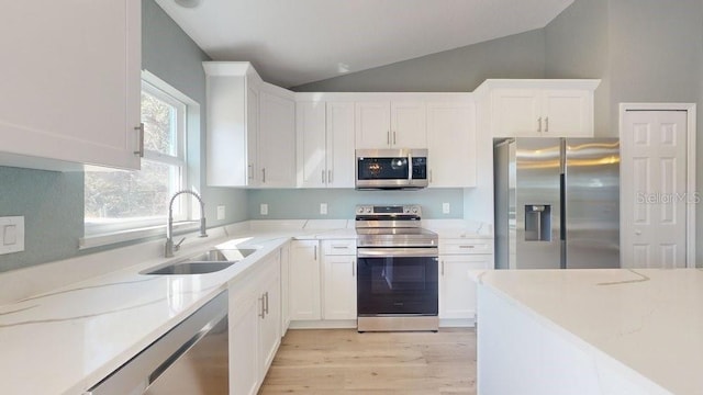 kitchen featuring lofted ceiling, sink, white cabinetry, light stone counters, and appliances with stainless steel finishes