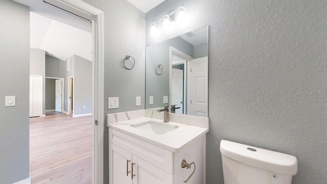 bathroom featuring vanity, hardwood / wood-style floors, lofted ceiling, and toilet