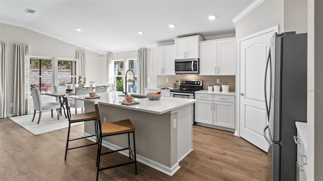 kitchen featuring white cabinets, appliances with stainless steel finishes, decorative backsplash, a kitchen island with sink, and vaulted ceiling