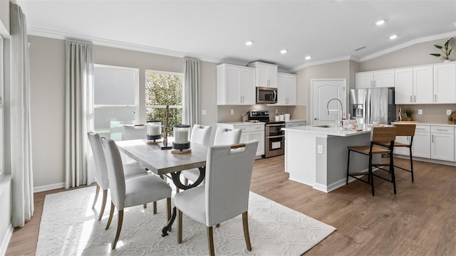 dining area featuring hardwood / wood-style flooring, sink, ornamental molding, and lofted ceiling