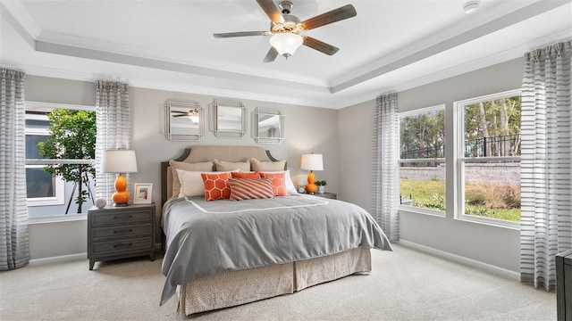 carpeted bedroom with ceiling fan, crown molding, multiple windows, and a tray ceiling