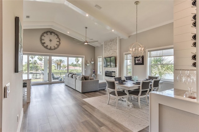 dining room featuring hardwood / wood-style floors, beam ceiling, high vaulted ceiling, a fireplace, and ceiling fan with notable chandelier