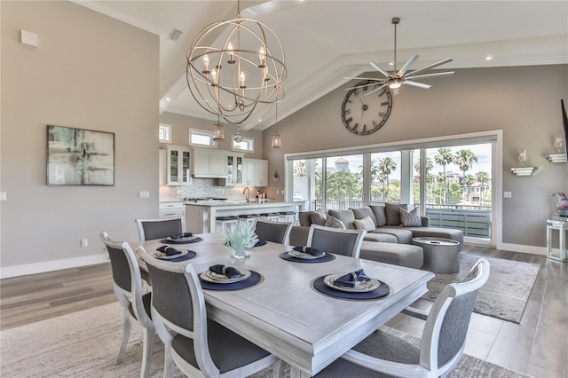 dining area featuring ceiling fan with notable chandelier, high vaulted ceiling, sink, and light hardwood / wood-style flooring