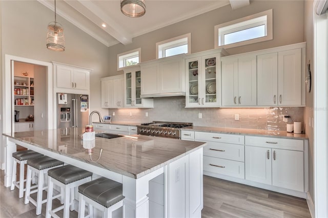 kitchen featuring high end fridge, backsplash, beam ceiling, and an island with sink