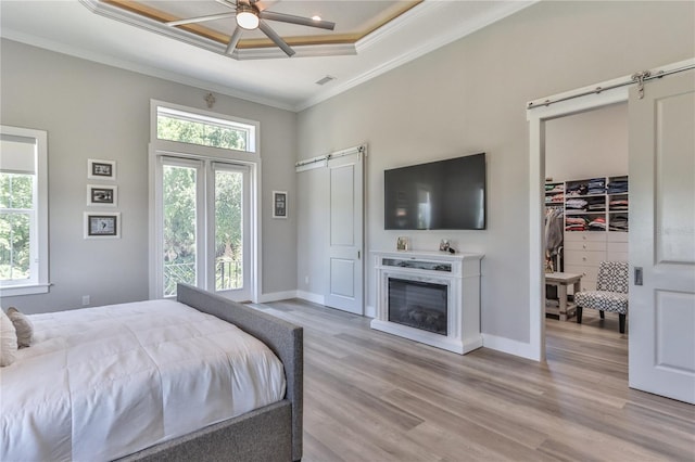 bedroom featuring crown molding, light hardwood / wood-style flooring, ceiling fan, a raised ceiling, and a barn door