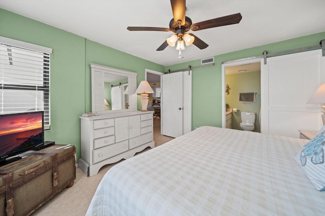 bedroom featuring a barn door, ceiling fan, and ensuite bath