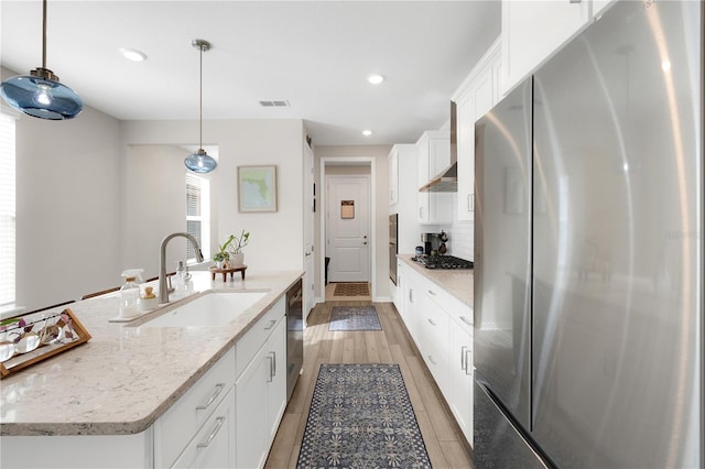 kitchen featuring sink, appliances with stainless steel finishes, hanging light fixtures, white cabinets, and a center island with sink