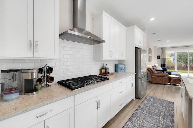 kitchen featuring wall chimney range hood, appliances with stainless steel finishes, light stone counters, tasteful backsplash, and white cabinets