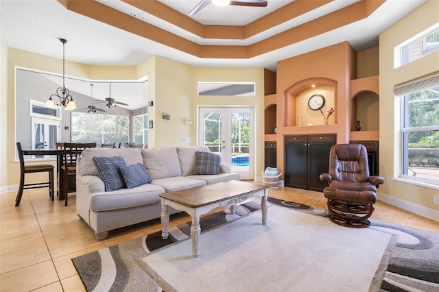 tiled living room featuring a tray ceiling, ceiling fan with notable chandelier, french doors, and a high ceiling