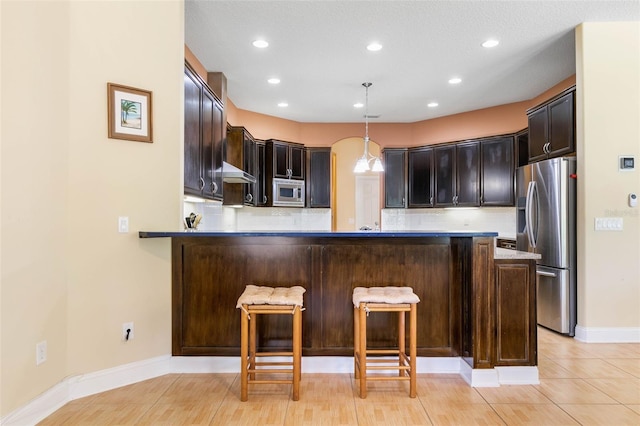 kitchen featuring appliances with stainless steel finishes, pendant lighting, tasteful backsplash, a breakfast bar area, and kitchen peninsula