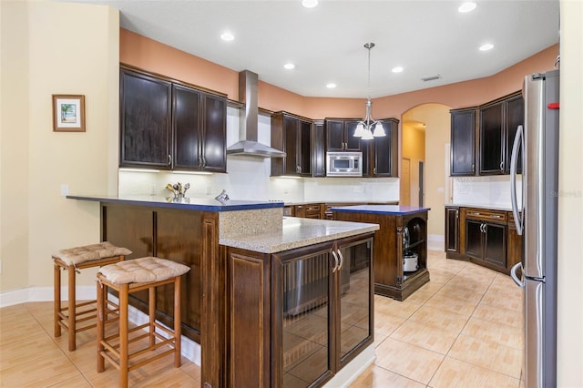 kitchen with a breakfast bar area, tasteful backsplash, hanging light fixtures, appliances with stainless steel finishes, and wall chimney range hood