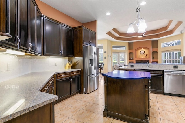 kitchen featuring hanging light fixtures, dark brown cabinets, light tile patterned floors, a tray ceiling, and stainless steel appliances