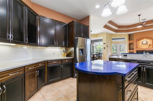 kitchen featuring stainless steel fridge with ice dispenser, a tray ceiling, decorative backsplash, and a kitchen island