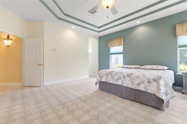 carpeted bedroom with a raised ceiling and ceiling fan