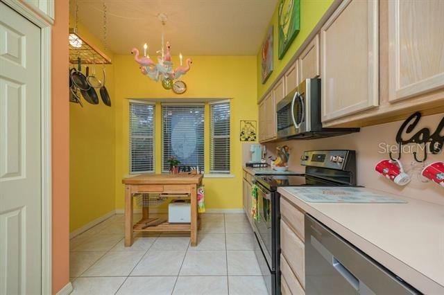 kitchen with light tile patterned floors, an inviting chandelier, stainless steel appliances, light brown cabinetry, and decorative light fixtures