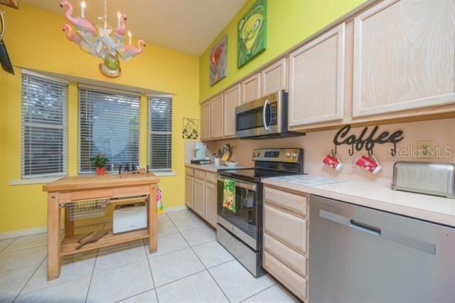 kitchen featuring an inviting chandelier, stainless steel appliances, light brown cabinetry, and light tile patterned floors