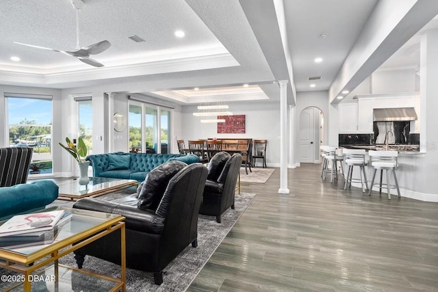 living room featuring ceiling fan, a raised ceiling, a textured ceiling, and ornate columns