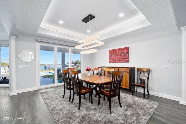 dining space featuring a raised ceiling, dark hardwood / wood-style flooring, and ornate columns