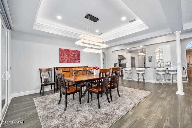 dining area with a tray ceiling, dark wood-type flooring, and decorative columns