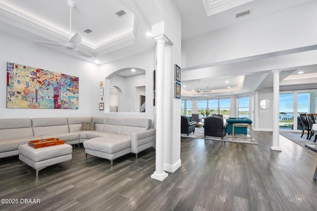 living room featuring dark hardwood / wood-style floors, ornamental molding, a tray ceiling, and ornate columns