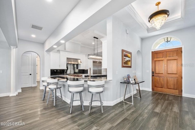 kitchen featuring a kitchen breakfast bar, white cabinets, dark hardwood / wood-style flooring, decorative light fixtures, and kitchen peninsula