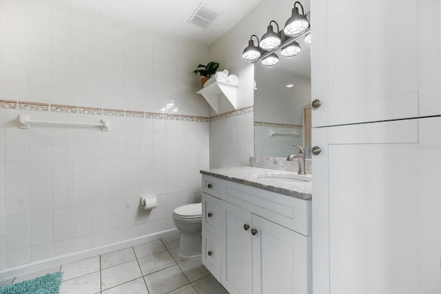 bathroom featuring tile patterned floors, vanity, toilet, and tile walls