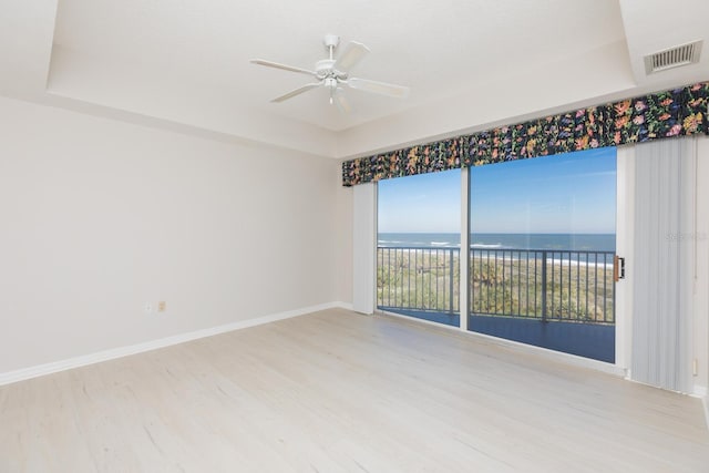 unfurnished room with a water view, ceiling fan, a raised ceiling, and light hardwood / wood-style floors