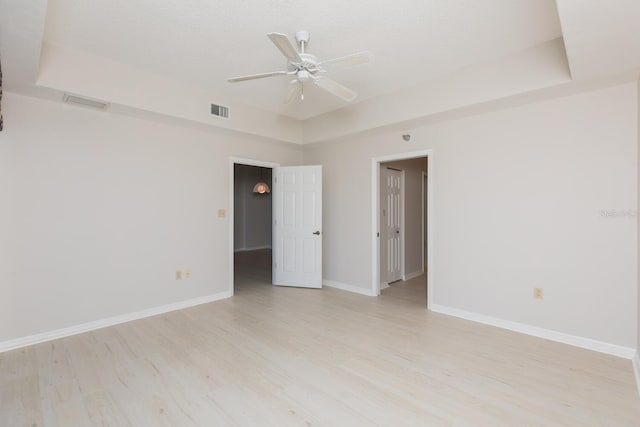 unfurnished room featuring a raised ceiling, a textured ceiling, ceiling fan, and light hardwood / wood-style flooring