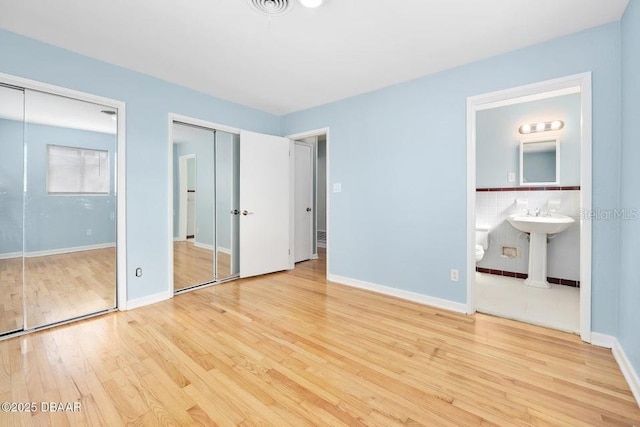 unfurnished bedroom with ensuite bathroom, two closets, tile walls, and light hardwood / wood-style flooring