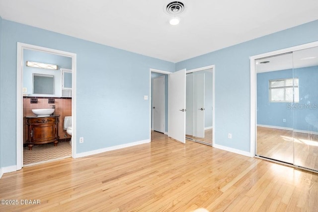 unfurnished bedroom featuring sink, connected bathroom, and light hardwood / wood-style floors