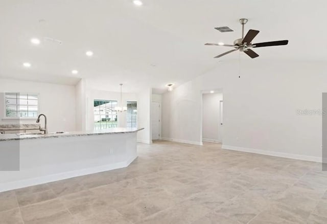 kitchen with light stone counters, open floor plan, hanging light fixtures, a healthy amount of sunlight, and a sink