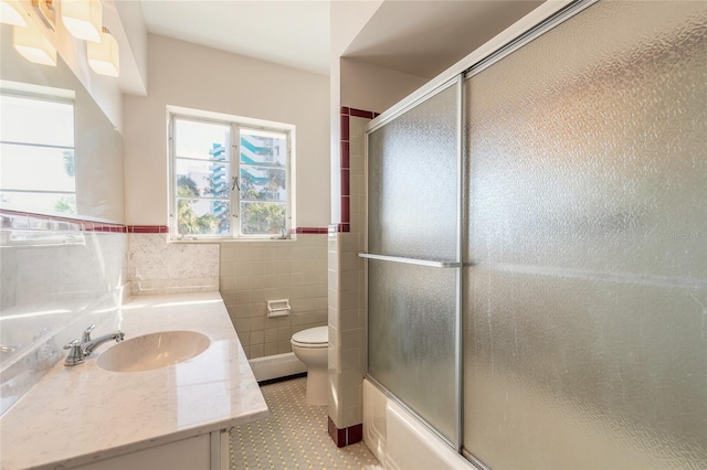 full bathroom featuring vanity, tile walls, bath / shower combo with glass door, and toilet