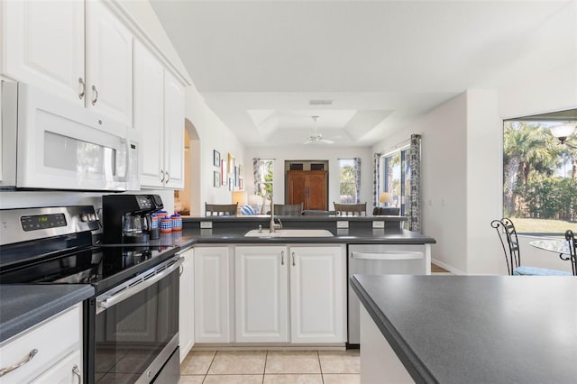 kitchen with light tile patterned floors, stainless steel appliances, a tray ceiling, white cabinets, and kitchen peninsula