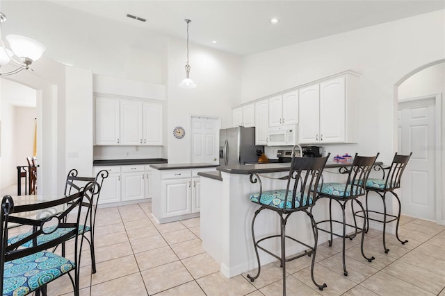 kitchen with white cabinetry, hanging light fixtures, light tile patterned floors, stainless steel fridge, and a kitchen island