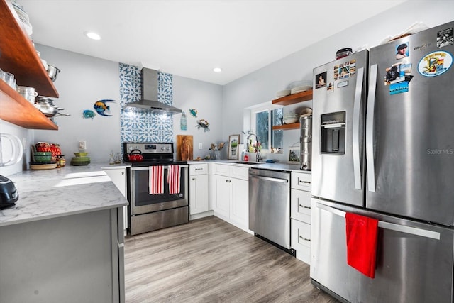 kitchen with appliances with stainless steel finishes, white cabinetry, sink, wall chimney range hood, and light hardwood / wood-style flooring