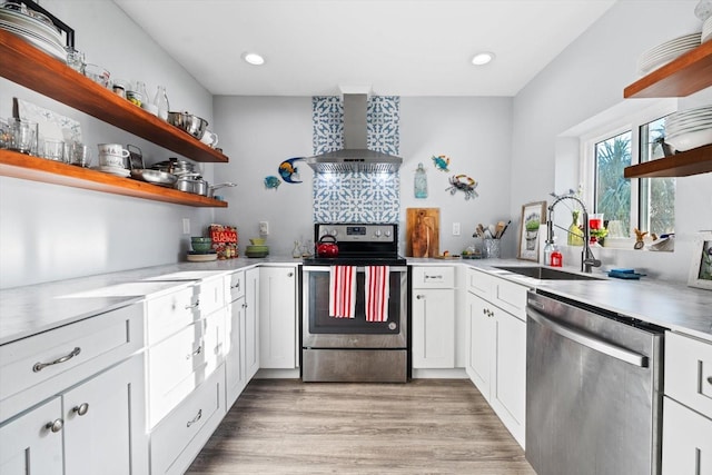 kitchen with sink, light hardwood / wood-style flooring, wall chimney range hood, stainless steel appliances, and white cabinets