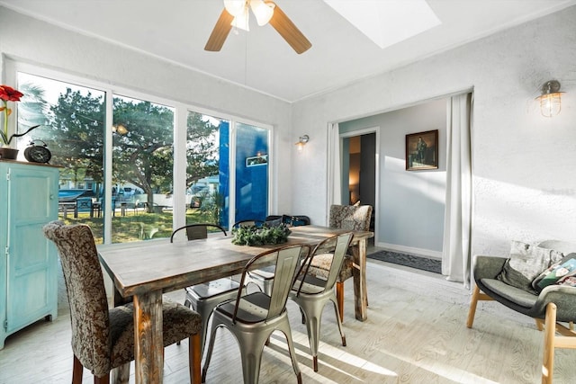 dining room with ceiling fan, a skylight, light hardwood / wood-style floors, and a wealth of natural light