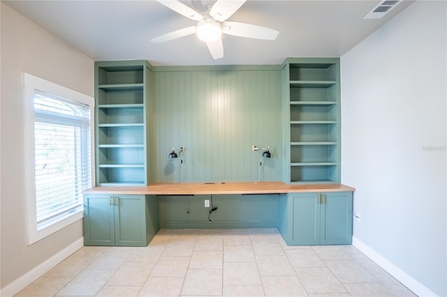 unfurnished office with light tile patterned floors, built in desk, ceiling fan, and built in shelves