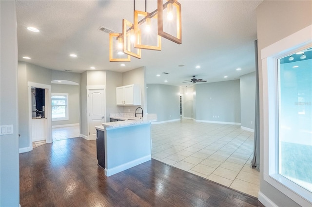 kitchen with hanging light fixtures, kitchen peninsula, hardwood / wood-style flooring, ceiling fan, and white cabinets