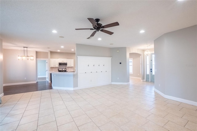 unfurnished living room featuring ceiling fan with notable chandelier, a textured ceiling, and light tile patterned floors