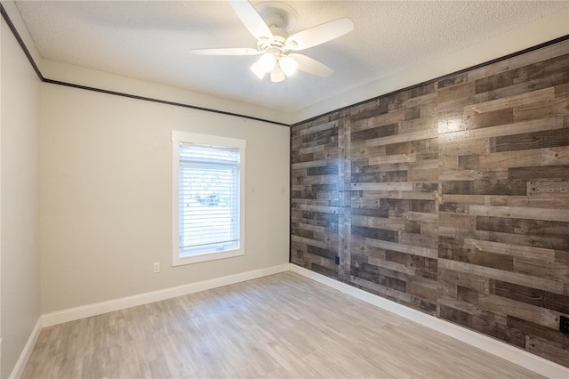 unfurnished room featuring ceiling fan, wooden walls, a textured ceiling, and light wood-type flooring