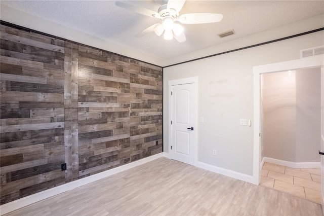 empty room with ceiling fan, wooden walls, a textured ceiling, and light hardwood / wood-style flooring