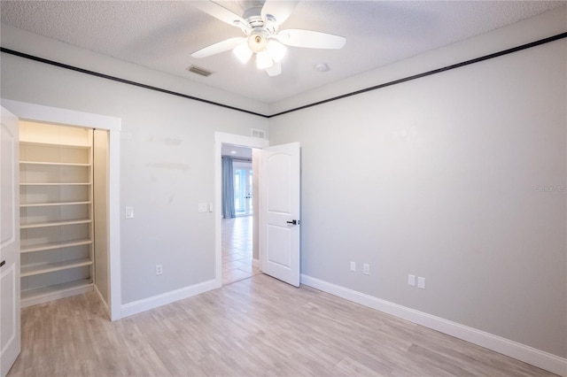 unfurnished bedroom with ceiling fan, a textured ceiling, a spacious closet, a closet, and light wood-type flooring