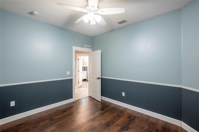 empty room with ceiling fan, dark wood-type flooring, and a textured ceiling