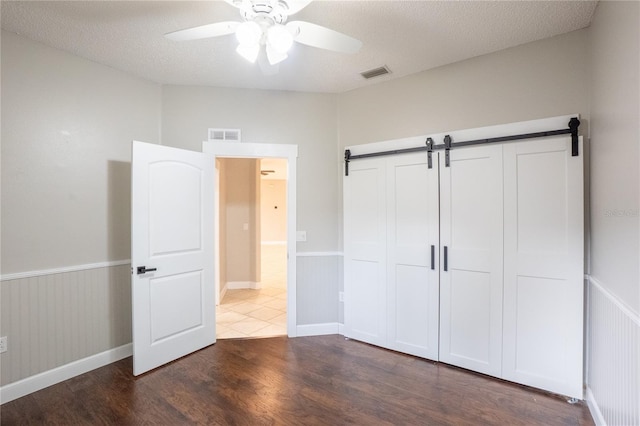 unfurnished bedroom featuring dark hardwood / wood-style flooring, ceiling fan, a barn door, a textured ceiling, and a closet