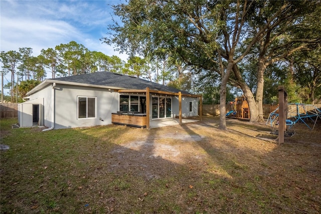 rear view of property featuring a playground, a patio, and a yard